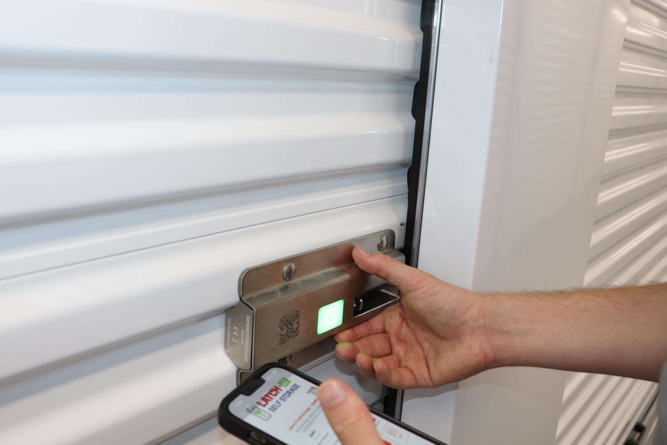 Person unlocking a storage unit with a keypad lock while using a smartphone for access.