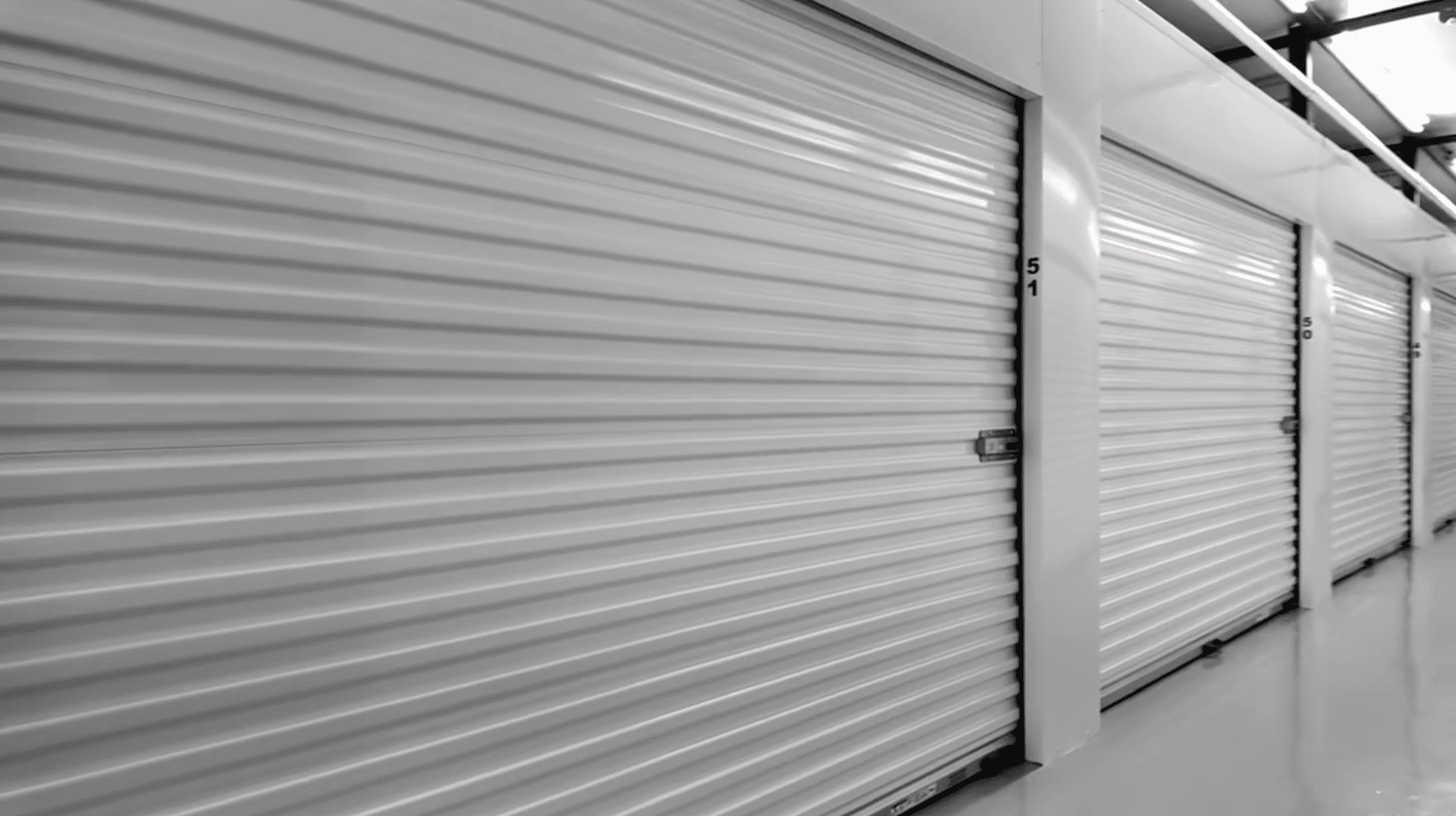 A row of indoor storage units with white roll-up doors and unit numbers.