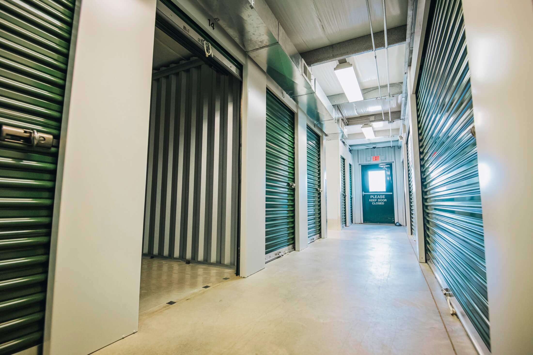 aisle of green indoor self storage units with one open