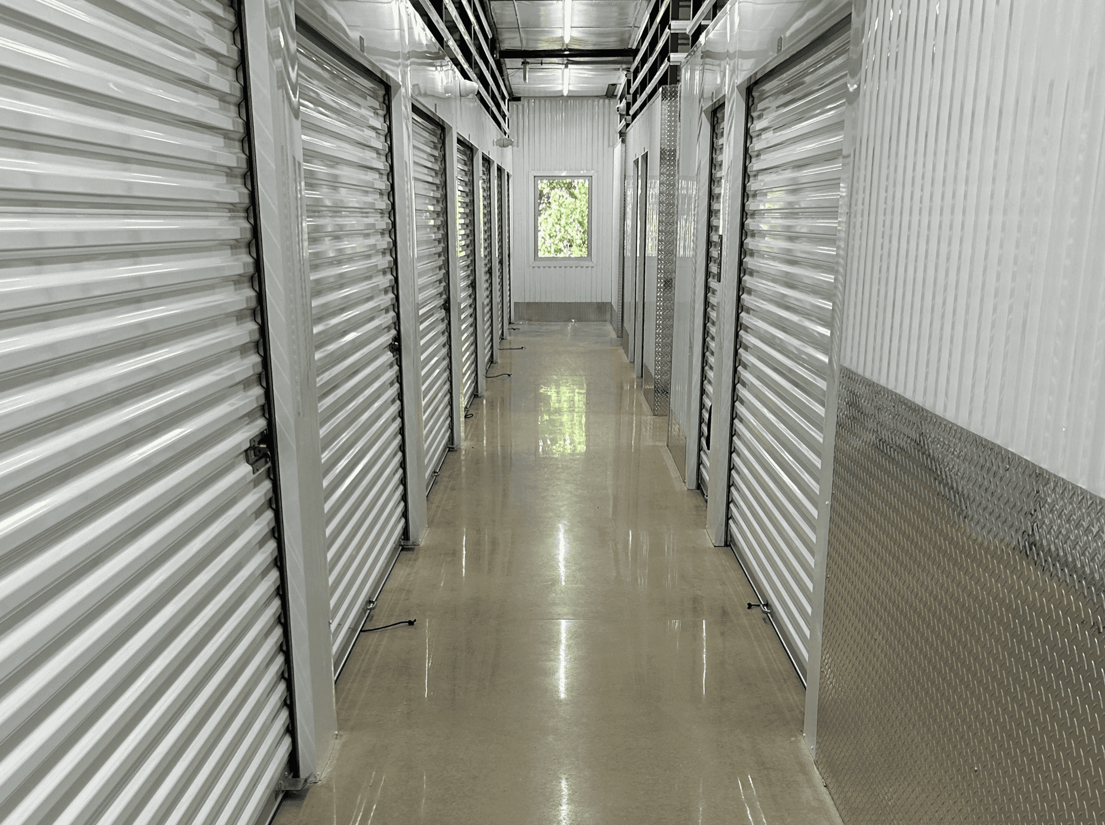 Long indoor hallway with metal storage units on both sides, a window at the end, and a polished concrete floor.