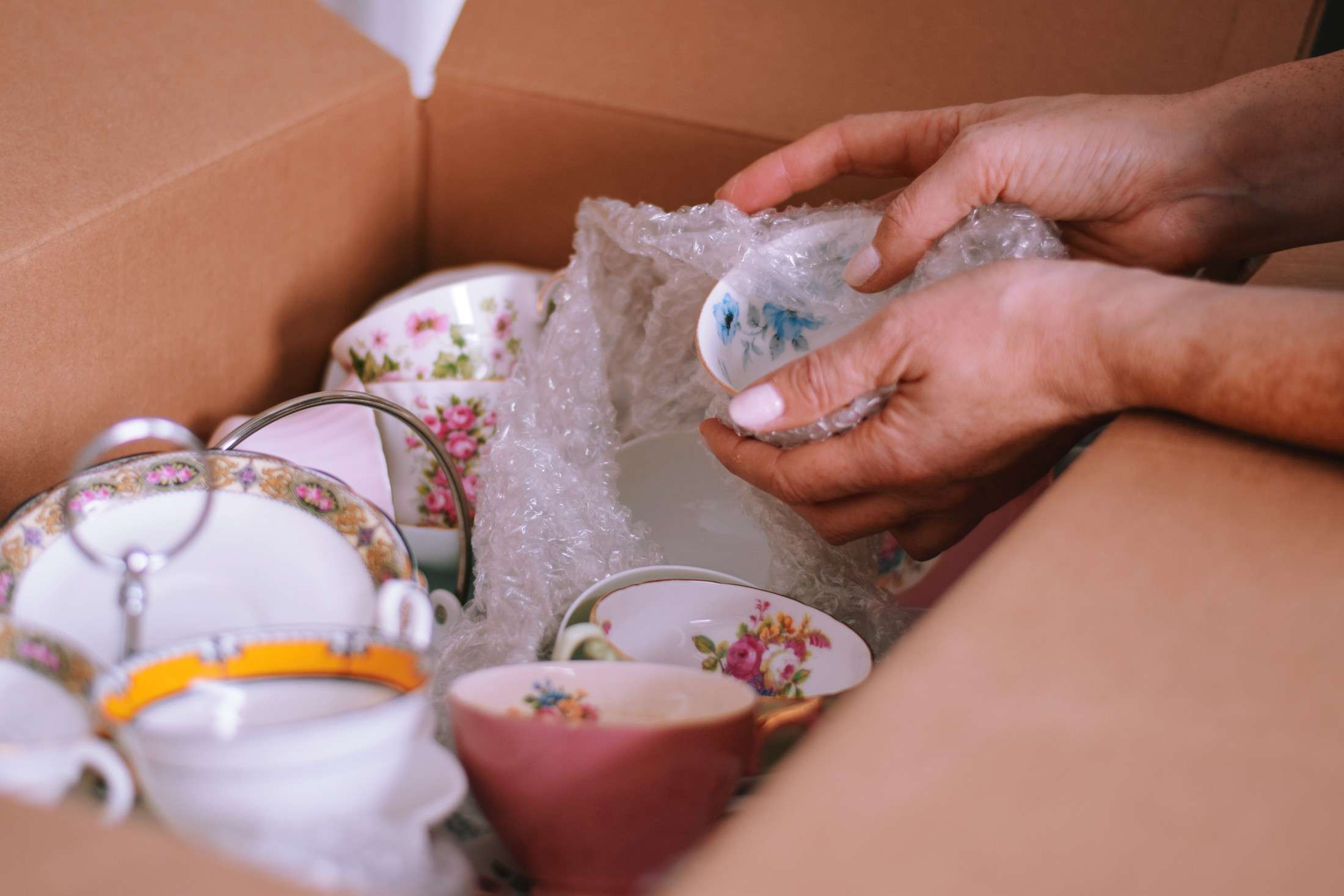 woman is packing fine china dishes into cardboard box