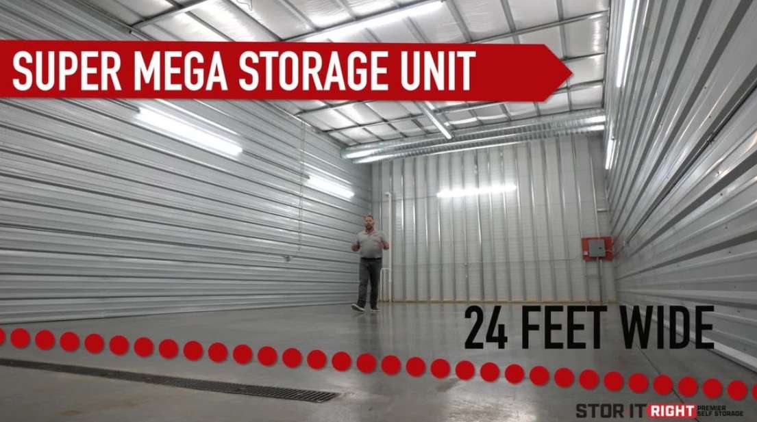 Huge metal storage unit with a man standing inside, labeled "Super Mega Storage Unit," 24 feet wide, with a red emergency box on the wall.